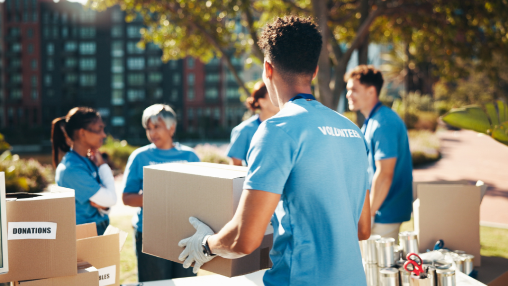 Team of volunteers in blue shirts organizing donation boxes at community event; Level 3 Social Prescribing professional qualification guide.