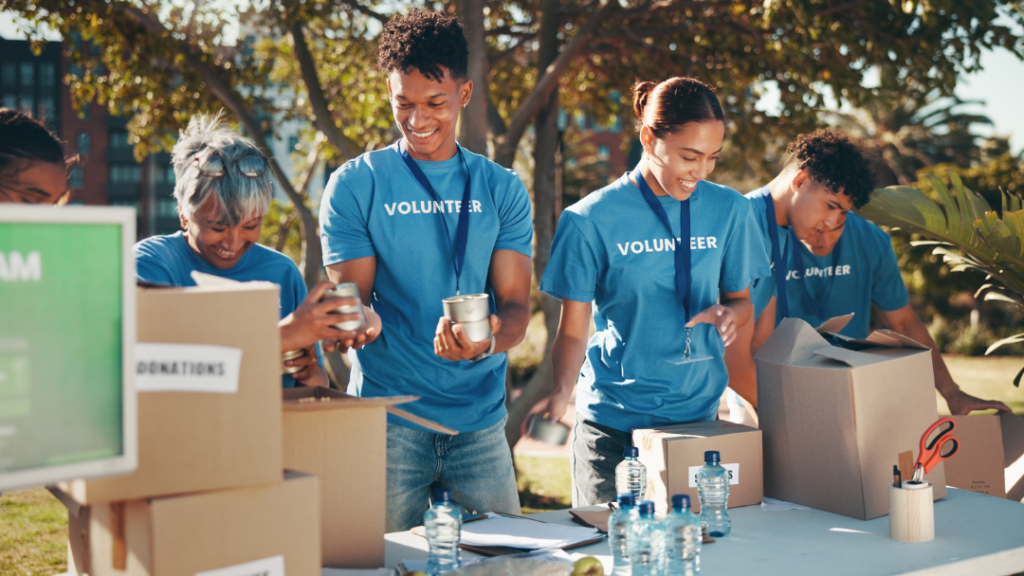 Diverse volunteer team in blue shirts packing donation boxes outdoors on a sunny day for community charitable organization.